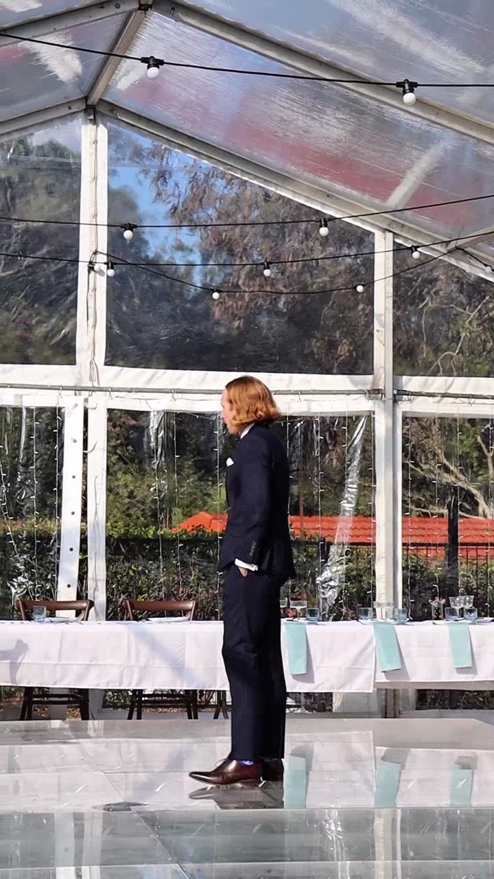 Groom standing alone under a clear marquee tent with string lights